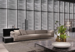 A living room setting is shown in a dim room with a backdrop of glowing panels with tube lights. In the living room is the new Echoo sofa and a coffee table with a floral presentation on top.