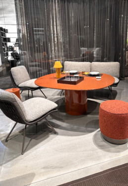 A lounging dining setting at the Minotti Pavilion in the Rho Fieramilano fairgrounds in Milan Italy - the largest and most popular furniture trade fair in the world, and quickly growing with over 360,000 attendees this year in 2024. This dining setting had one low table in a deep burnt orange, and four seats - two lounge chairs, an ottoman, and one lounge love seat.