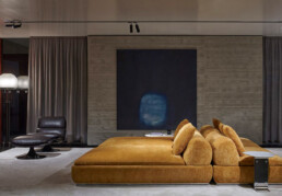 A large yellow seating system sits centre to the image, while a black armchair is to the left of it in a dimly lit room - the Minotti Pavilion during Salone del Mobile 2024