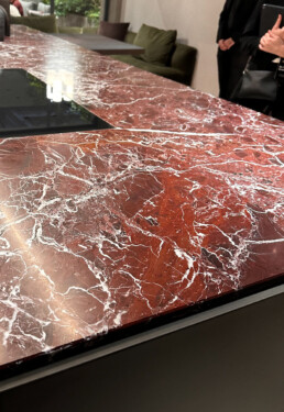 An up-close and personal photo of a kitchen counter top in a beautiful rhubarb red marble with white veining and deep maroon hues.