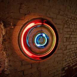 An art display on a wall in a dark wall. The piece appears to be a large multi-coloured flowing neon tube.